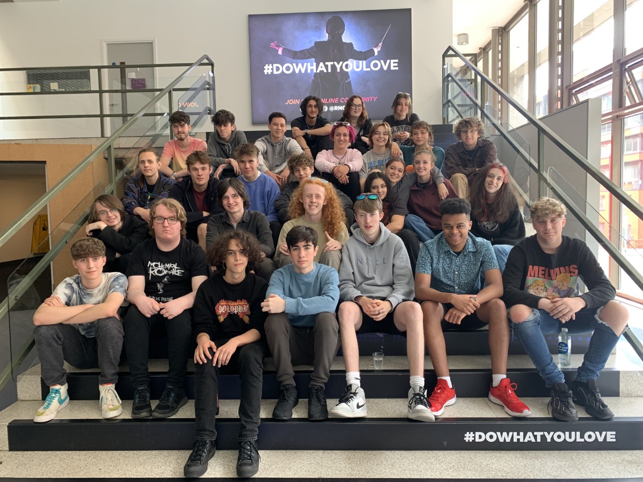 Class of Junior RNCM 2022, which is made up of teenagers in casual clothing, sit on stairs at the RNCM.