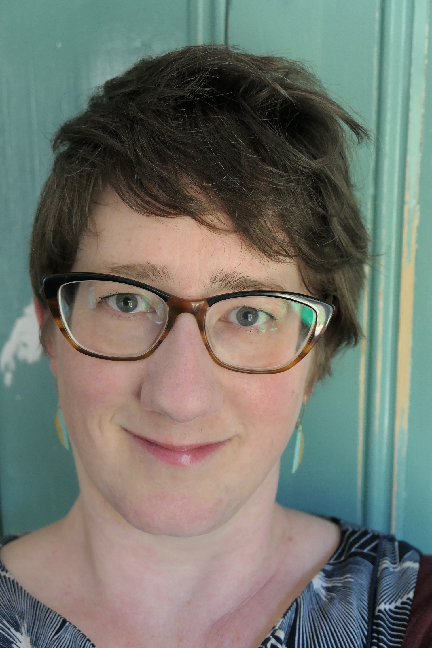 A headshot of a person with short dark hair wearing glasses.