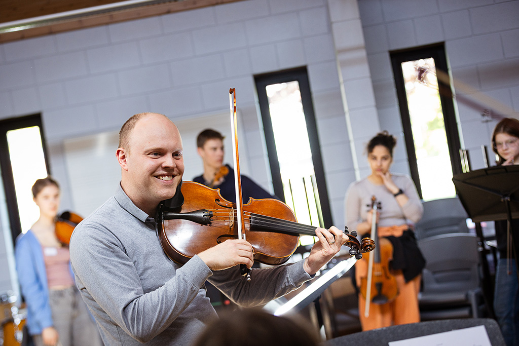 An RNCM lecturer plays the violin in front of a group of students.