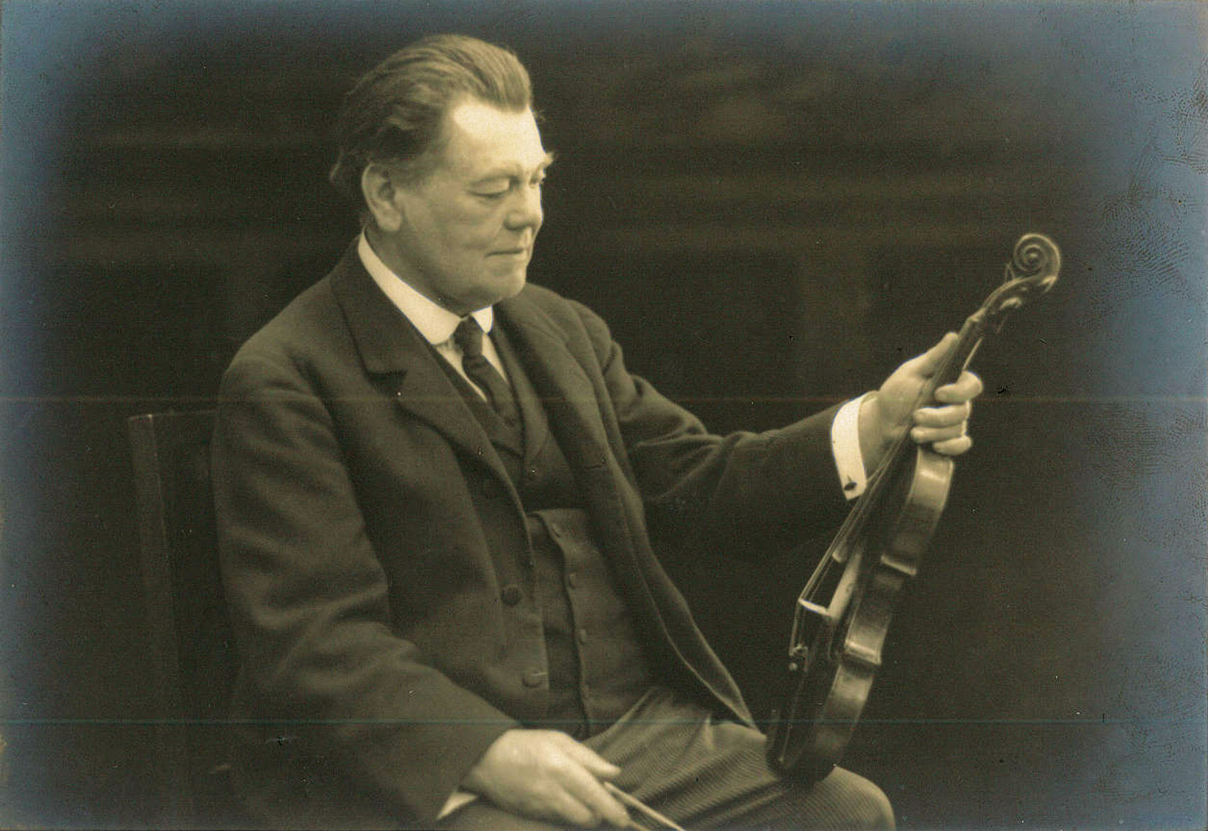 Adolph Brodsky sitting with a violin.