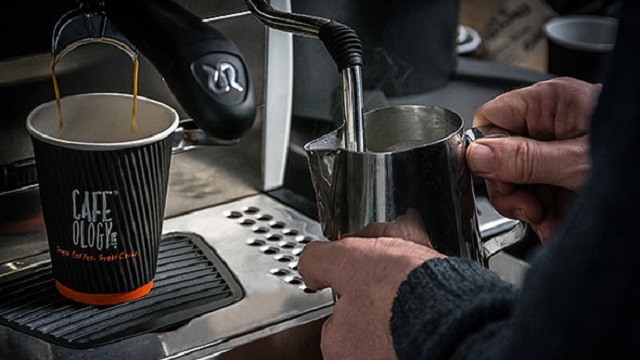 Close up of someone's hand holding a milk jug standing at a coffee machine