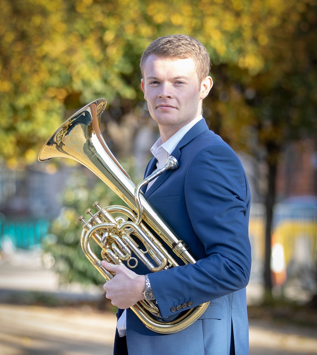 Mike Cavanagh facing the camera in a blue blazer holding a baritone horn