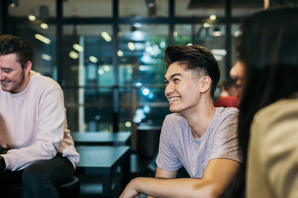 A group of three students sit around a table socialising. 