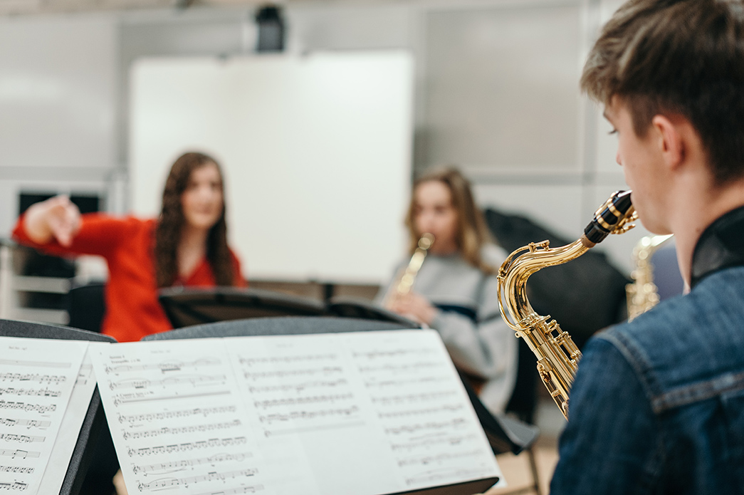 A young saxophone player sits in front of his sheet music and plays his instrument.