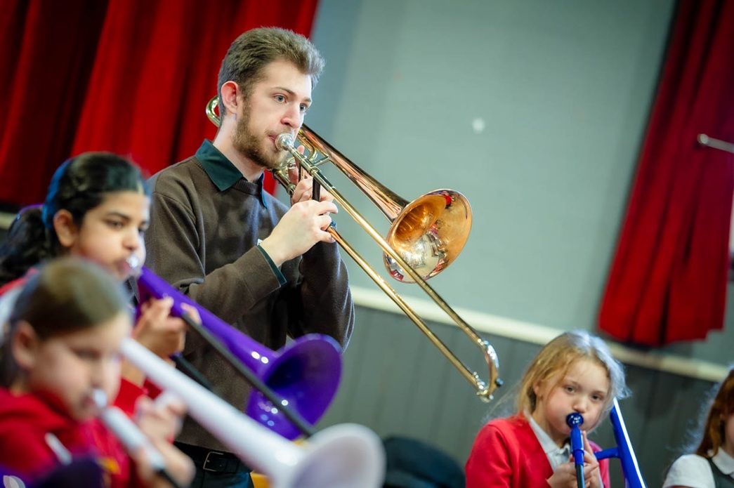 Trombone tutor playing the trombone with a few schoolchildren. 
