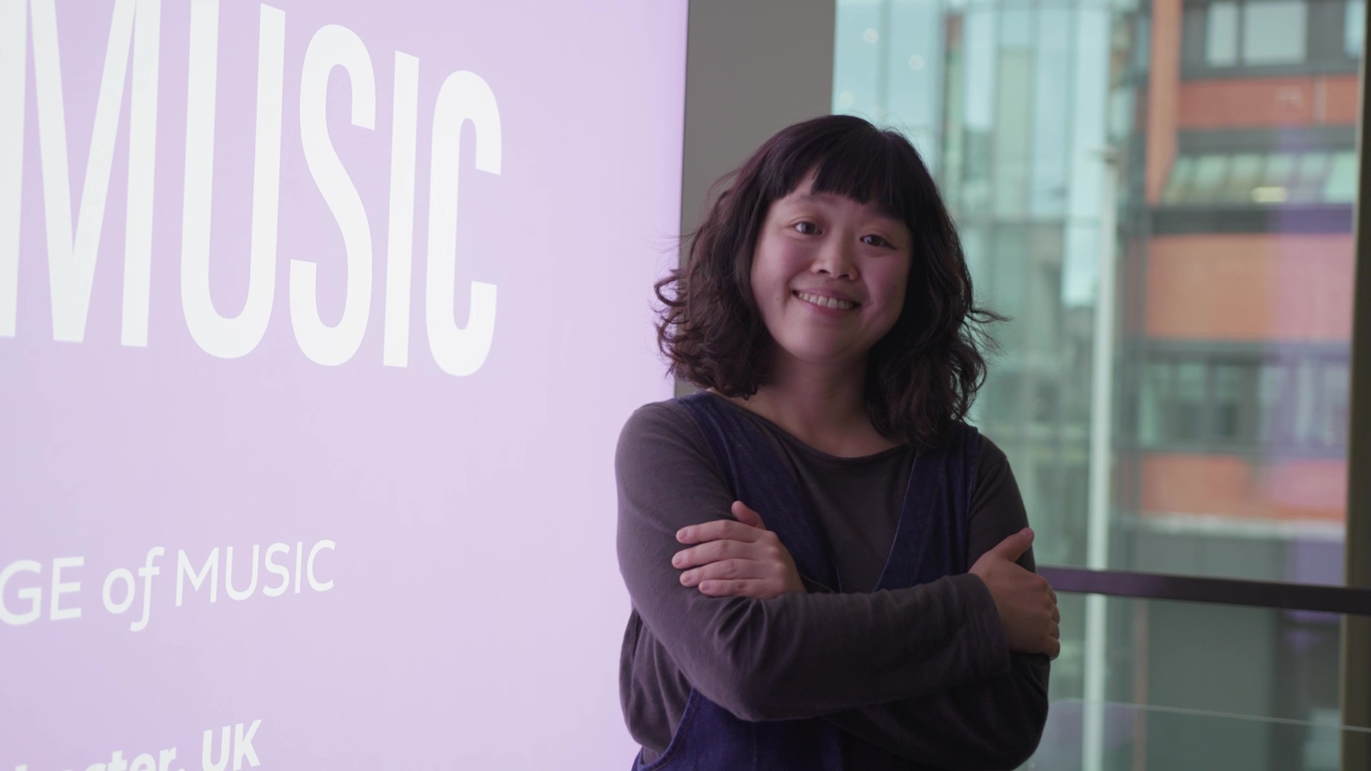 Jo Yee Cheung standing with arms folded next to a poster with the word music on it