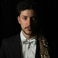 Male wearing black tie suit and holding saxophone