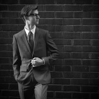 Black and white photo of male in suit against brick wall