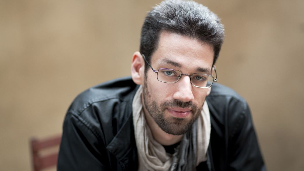 Male with glasses and short dark hair sitting on a chair