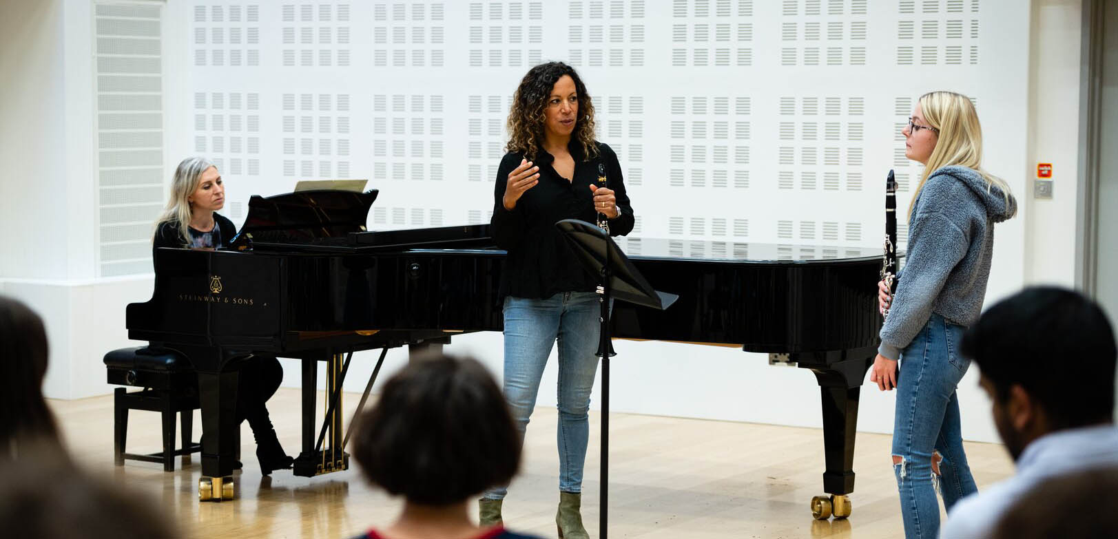 A student and tutor stand talking in front of a music stand holding clarinets as part of a class. 