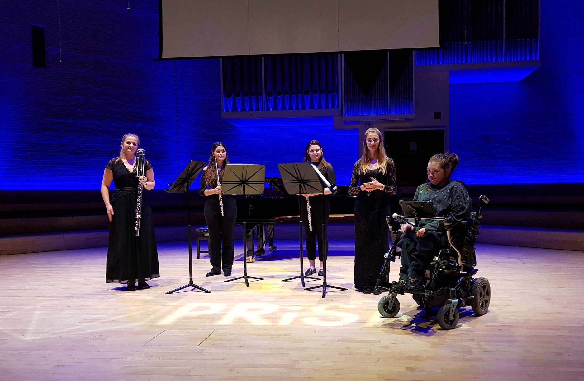 A young woman in a wheelchair with four flute players on stage