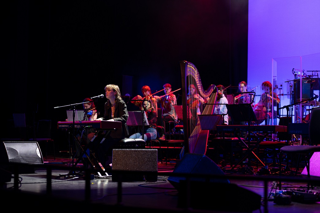 May Payne playing piano with orchestra behind