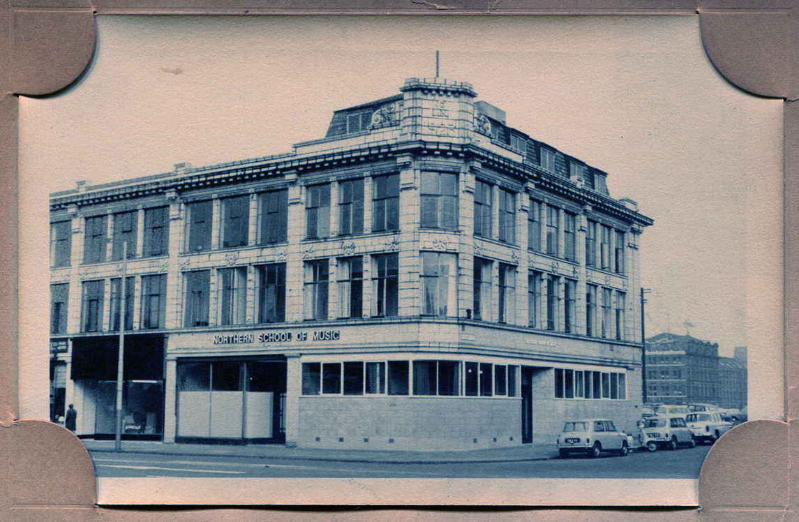 Old photograph of the Northern School of Music building with Mini's parked in front.