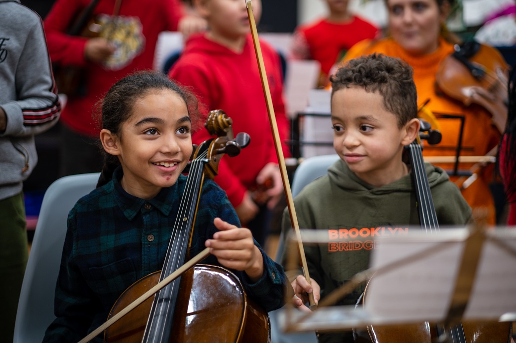 2 smiling children holding violins 