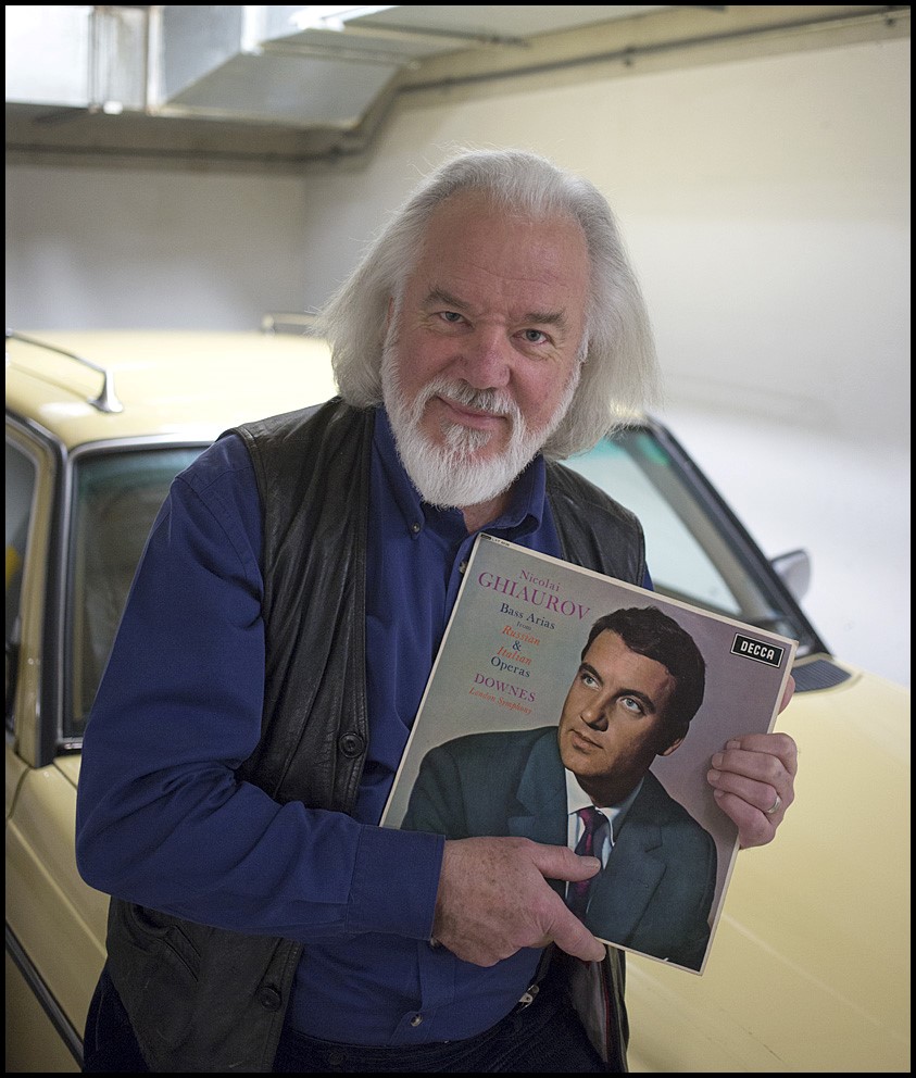 Sir John Tomlinson holding a vinyl LP by Nicolai Ghiaurov, standing in front of a car.