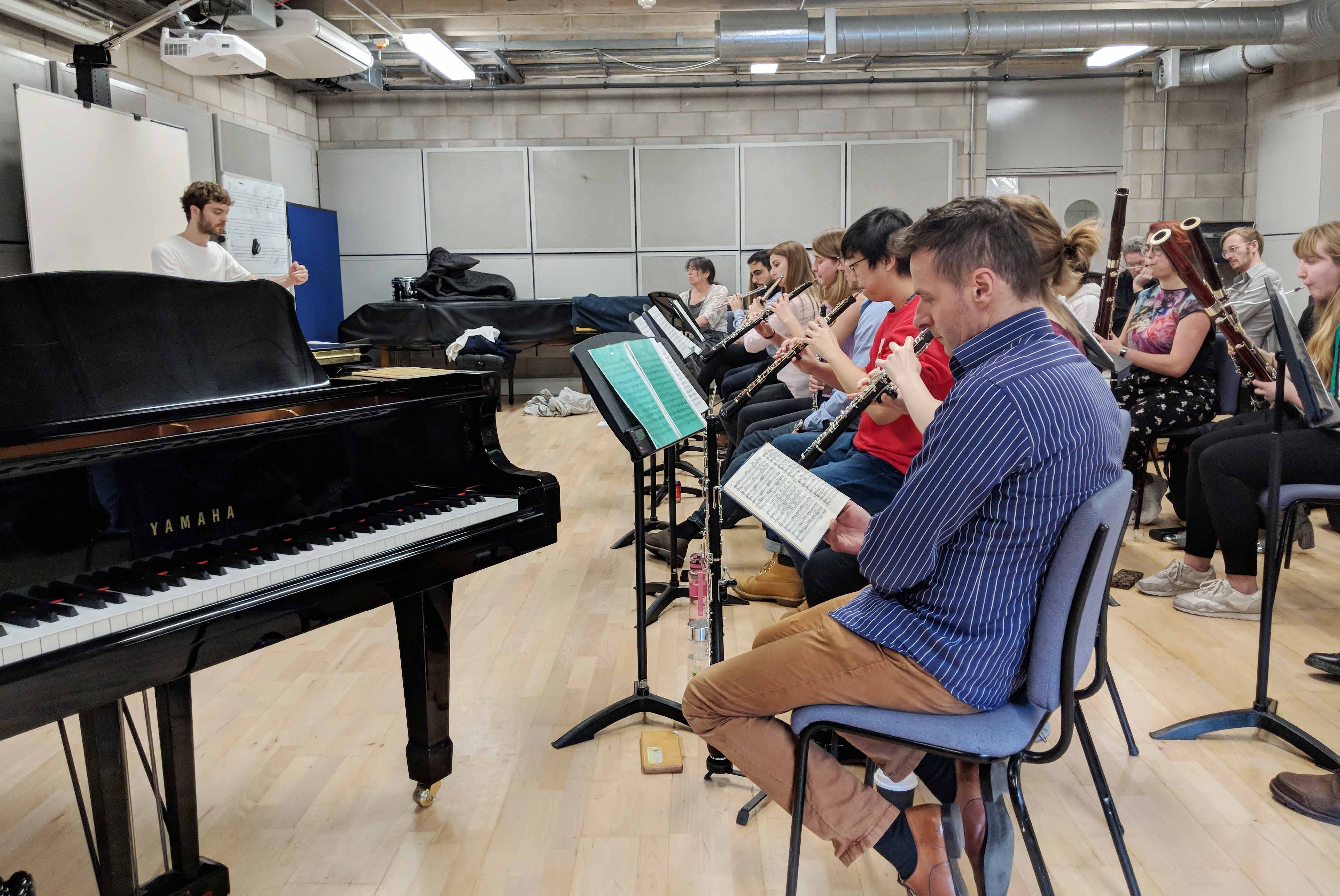 An orchestra consisting of oboes and clarinets rehearse in a studio. 