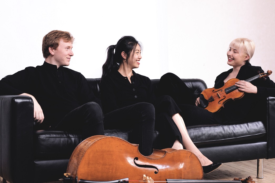 Paddington Trio sitting on a couch with their instruments.