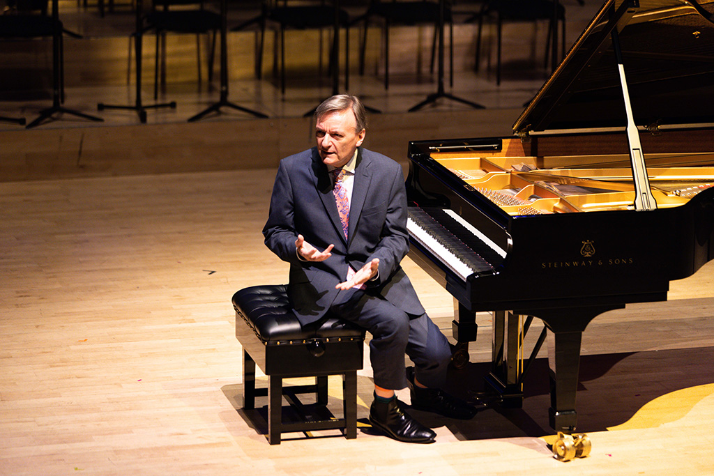 Sir Stephen Hough sits at a piano talking to an audience.