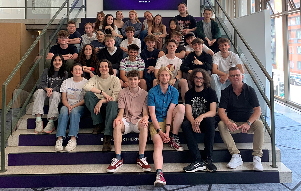A large group of the students from the 2025 Pop summer school sit on the stairs of the RNCM.