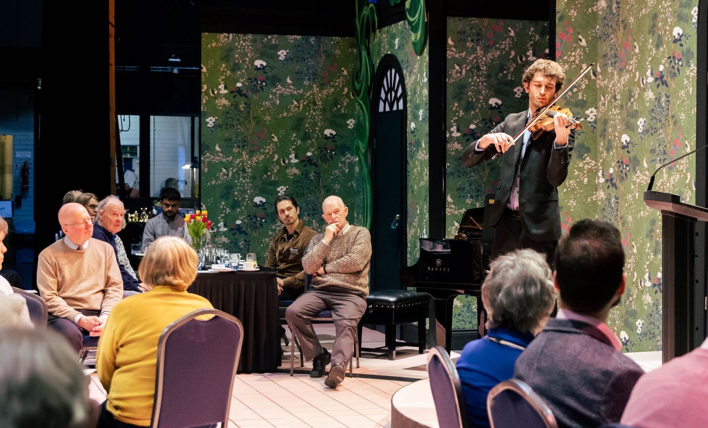 Photo of a violinist performing to a small group sitting around tables.