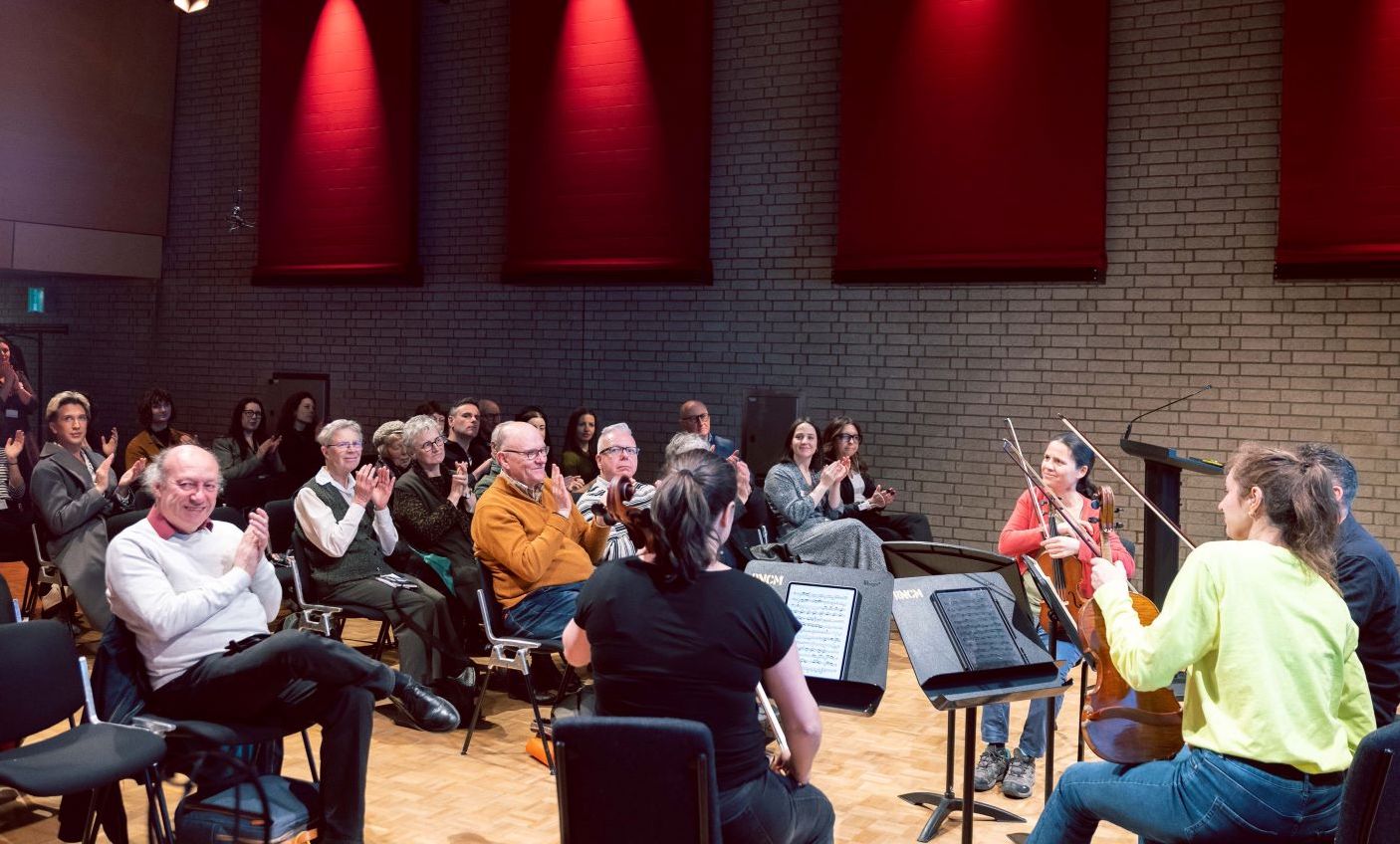 Photo of a small audience applauding a string quartet in a small concert hall.