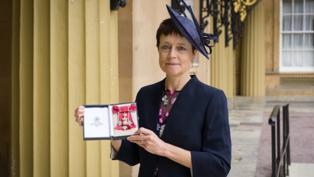 Professor Linda Merrick with her CBE standing outside Buckingham Palace