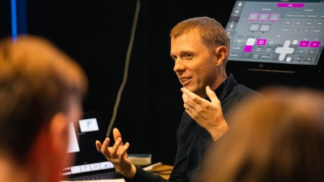 RNCM tutor with his hands up gesturing to a room of people