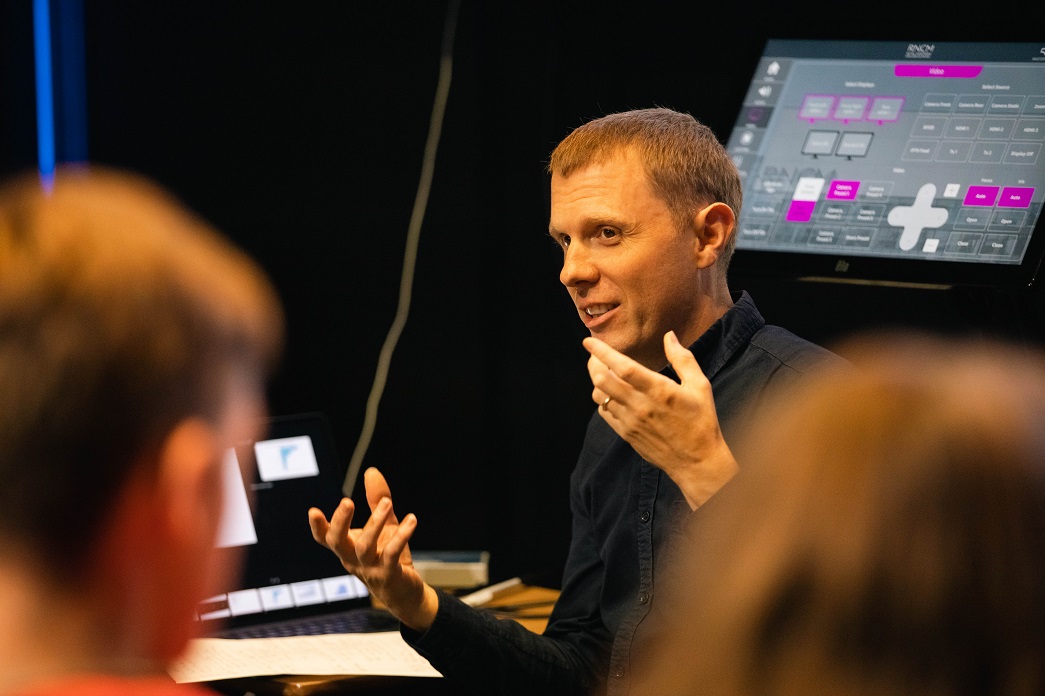 RNCM tutor with his hands up gesturing to a room of people