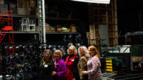 A group of five women stand in a line backstage. 