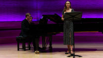 A singer and pianist perform together on stage. 