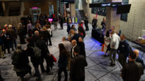 People stand on the RNCM concourse socialising. 