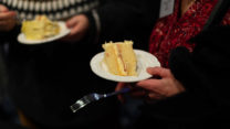 A hand holds a plate with a piece of cake. 