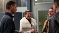 A group of four alumni stand in a circle laughing. 