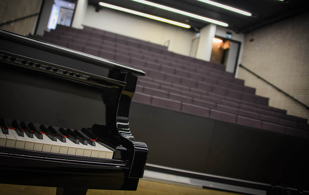 A piano stands in an empty lecture theatre.