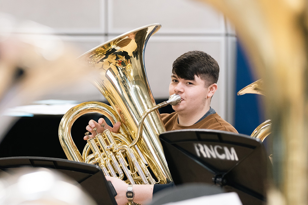 A student is playing the tuba surrounded by music stands.