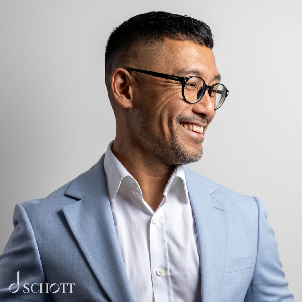 Raymond Yiu looking to the side smiling. He is wearing a white shirt and pale blue blazer.