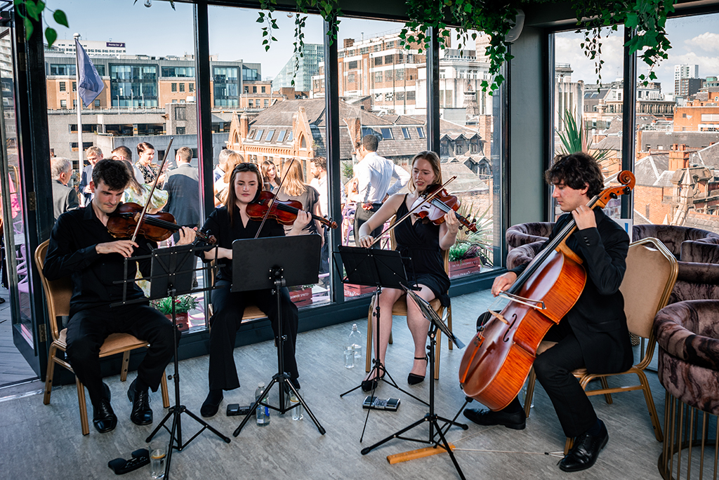 A string quartet play in front of a large window. 