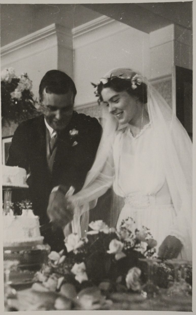 Old photograph of smiling bride and groom cutting wedding cake.
