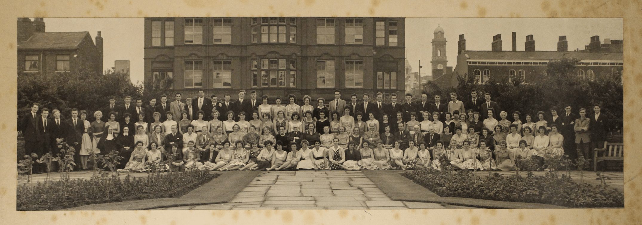 Large group picture of students, tutors and nuns outside dressed in suits and dresses.