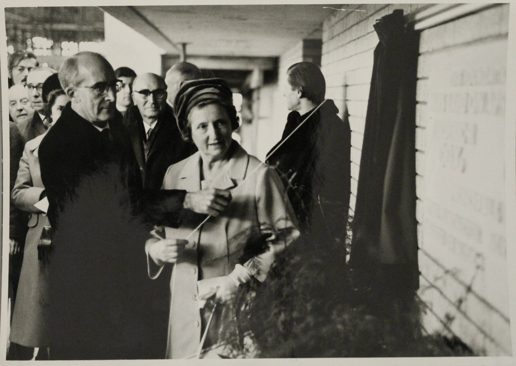 A man and woman unveiling of the RNCM foundation stone with a crowd of people behind them.