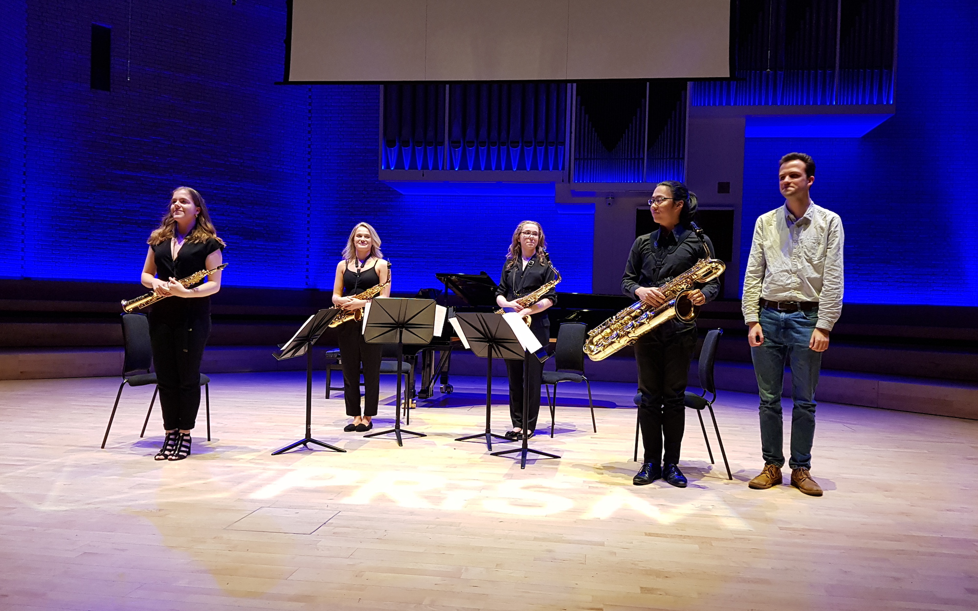 4 saxophone players on stage with a young man