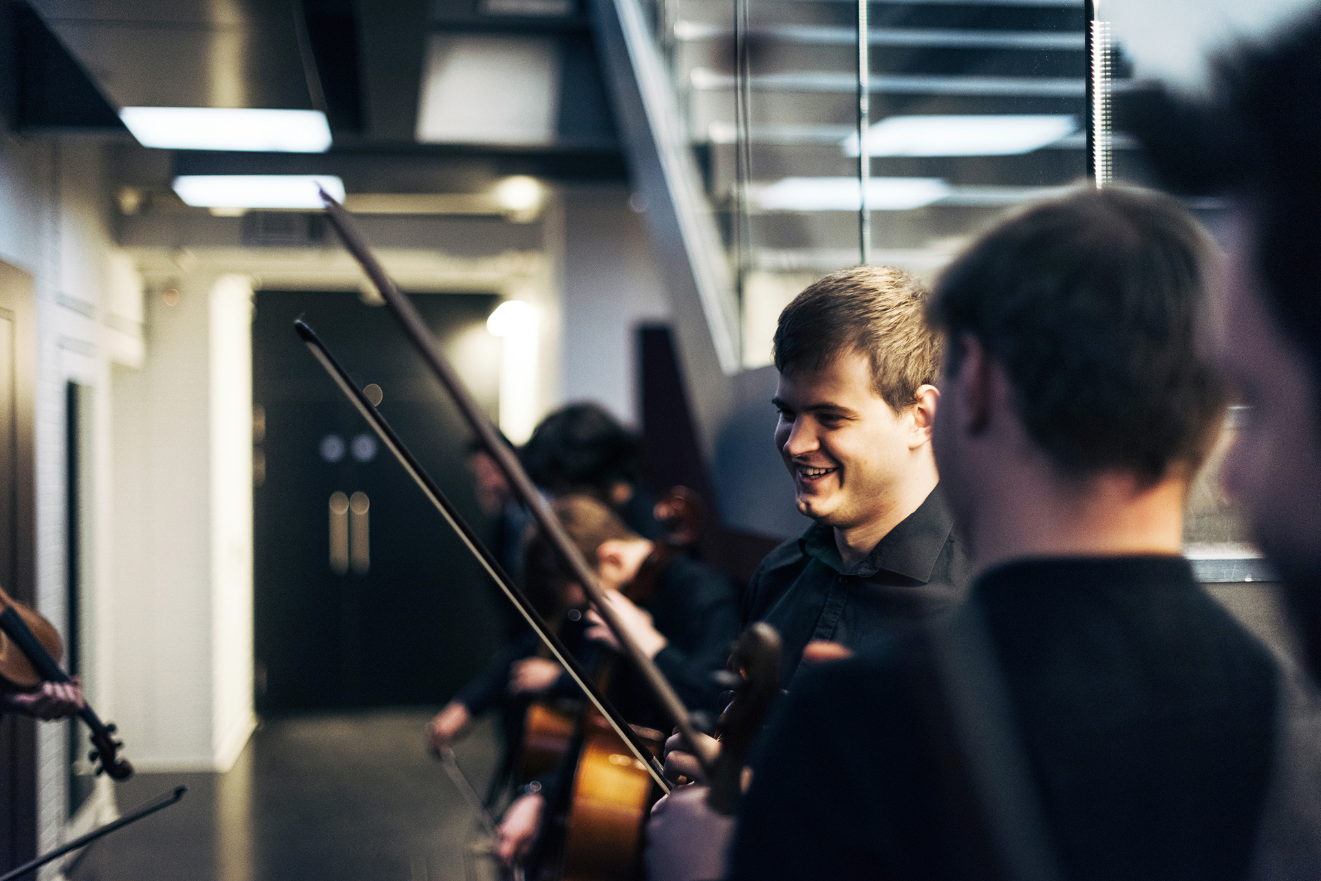 RNCM students holding stringed instruments wait in a line backstage. 