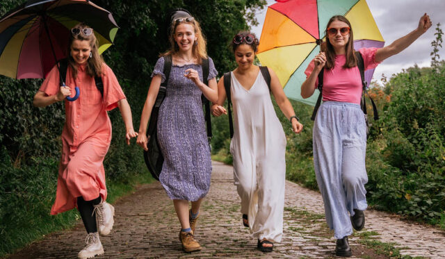 Four woman walk down a country path holding colourful umbrellas.