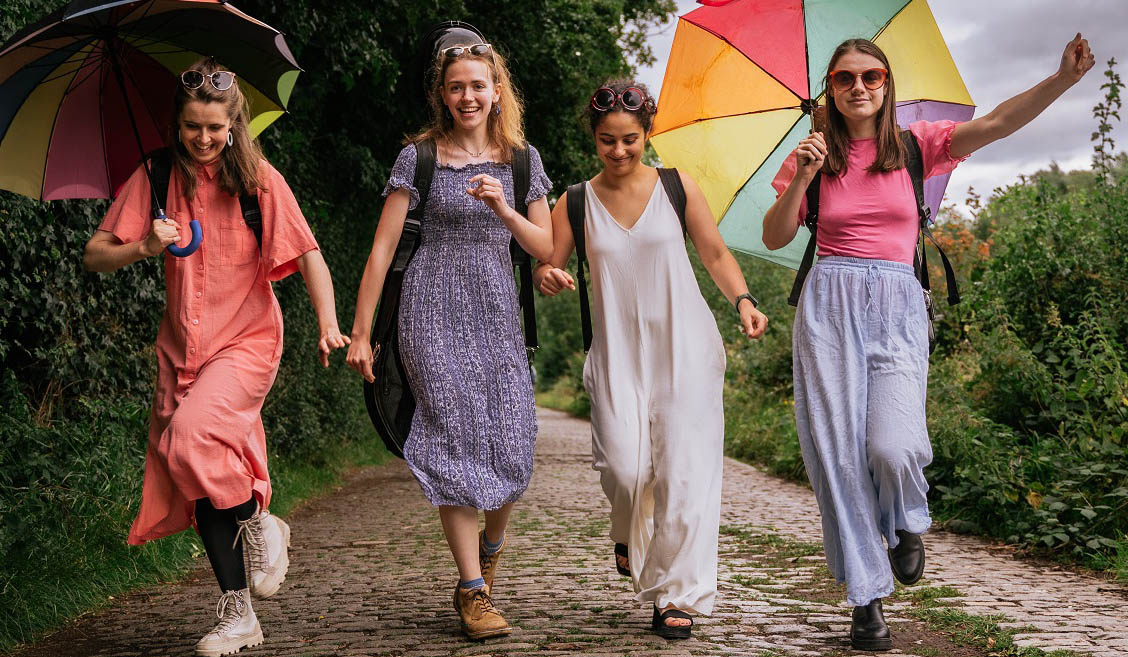 Four woman walk down a country path holding colourful umbrellas. 