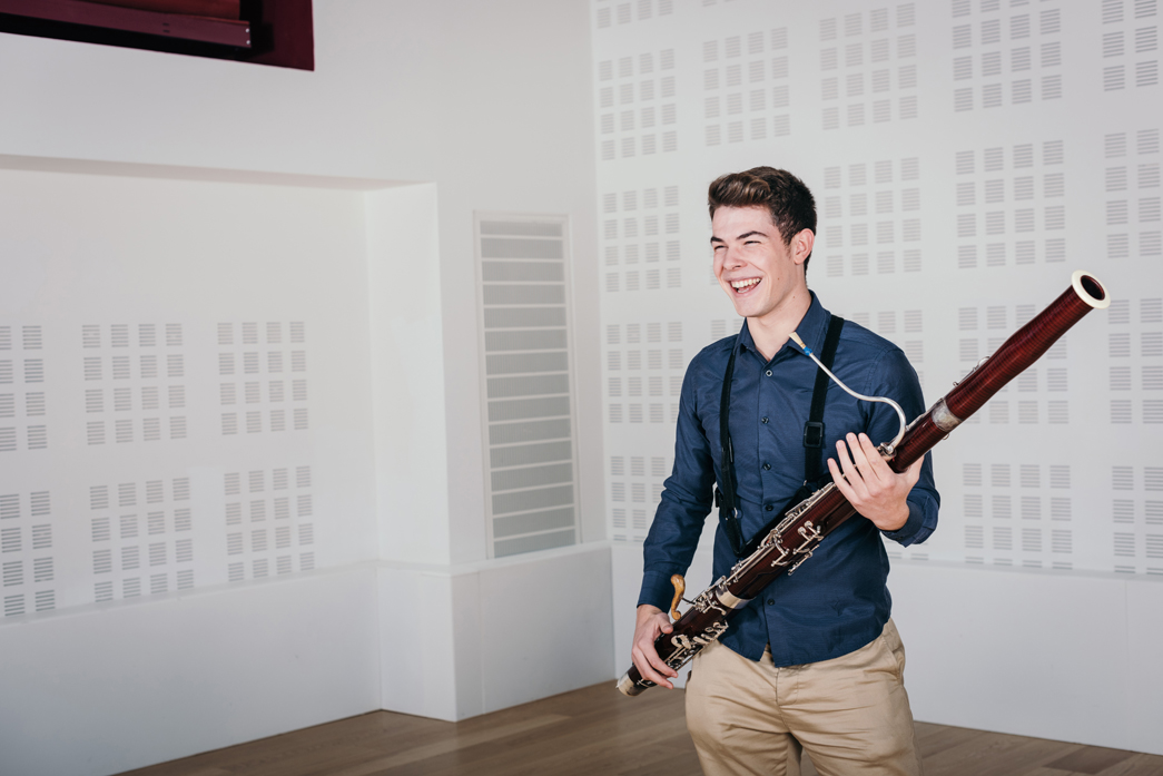 An RNCM student laughs while holding a bassoon in a studio.