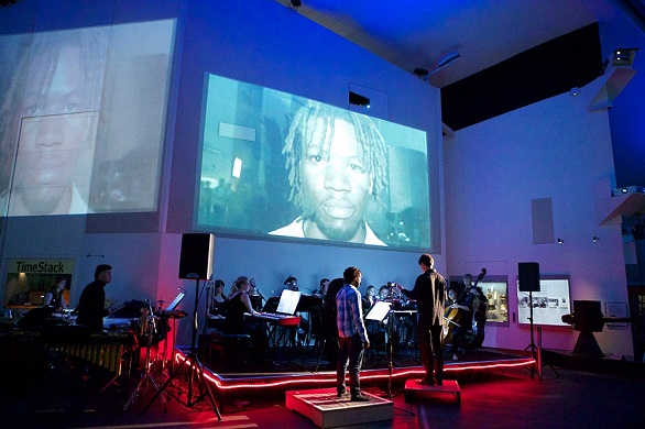 A small orchestra play in front of projections as part of the From Street to Trench exhibition. 