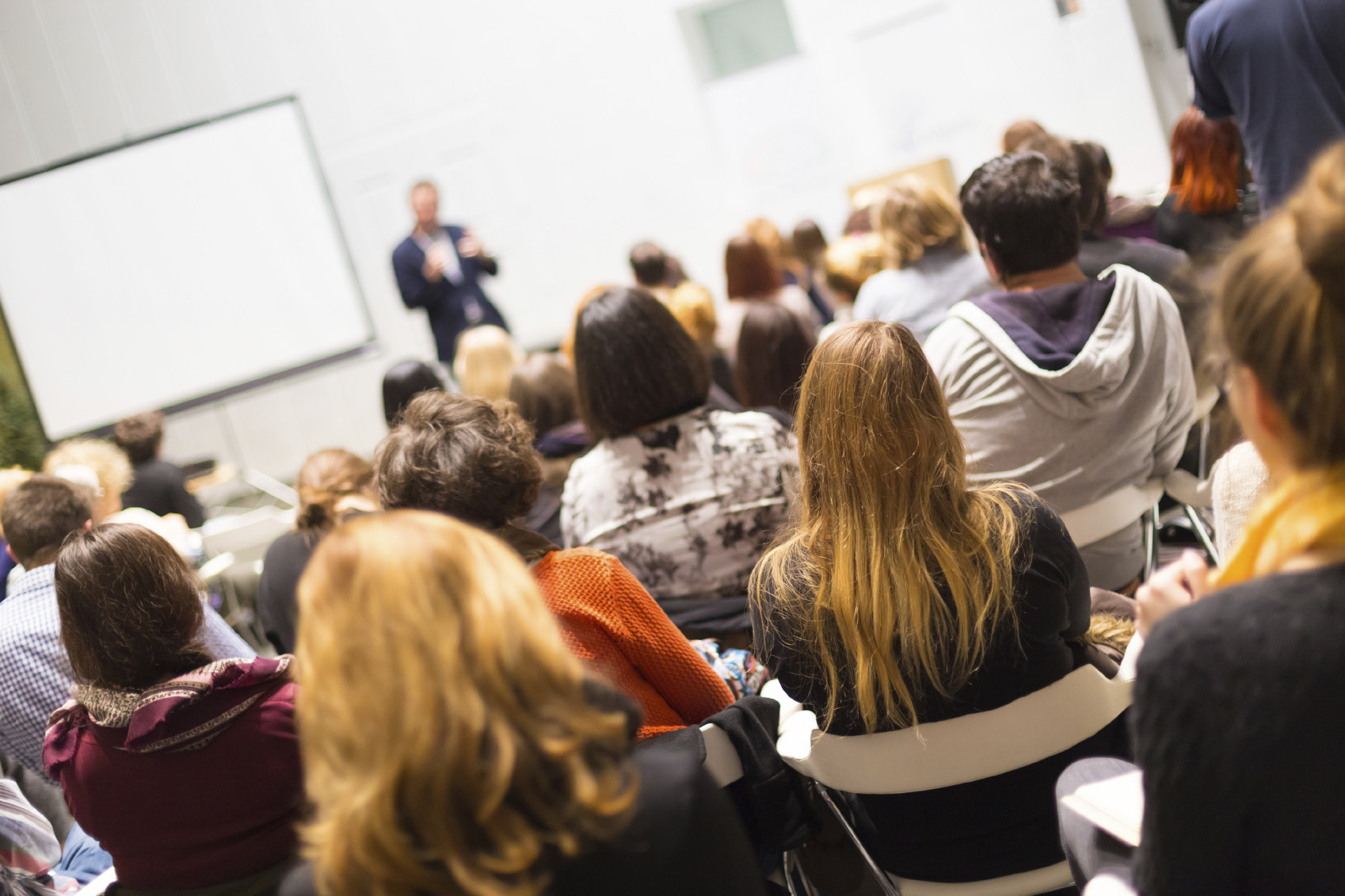 A speaker is giving a talk in a busy conference hall.