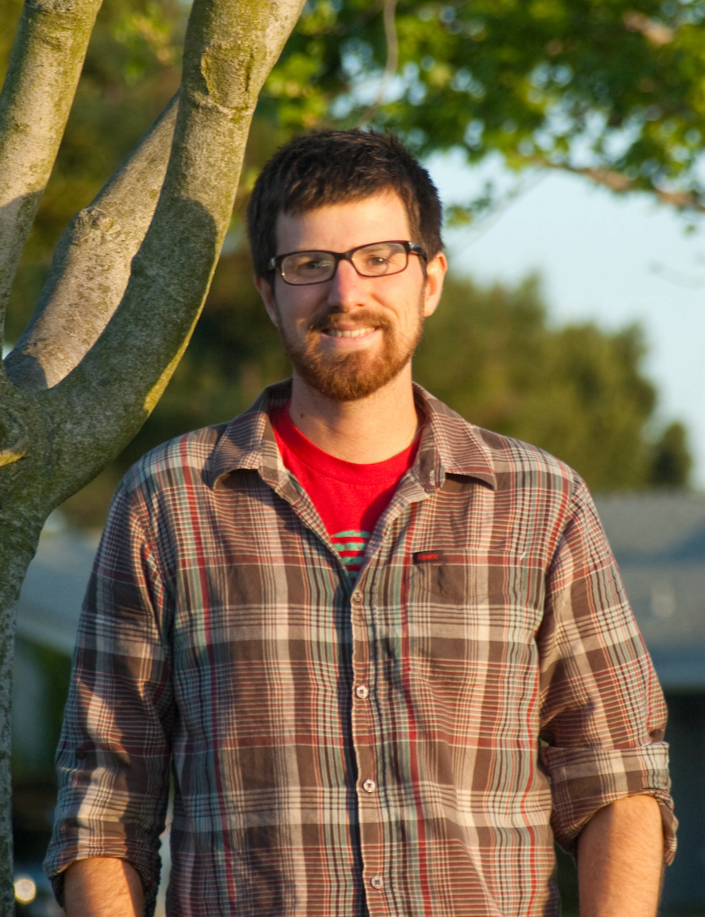 A man standing outside in a red check shirt and glasses