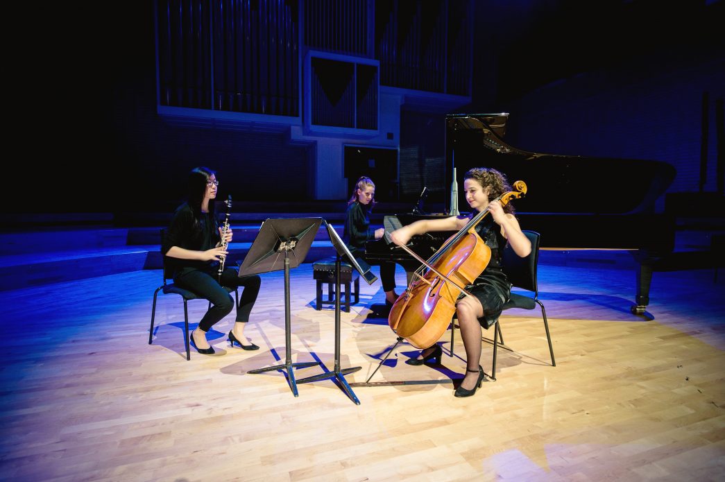 A pianist, clarinettist, and cellist perform together in the RNCM theatre. 