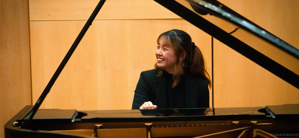 Student pianists sitting at a grand piano with the lid up
